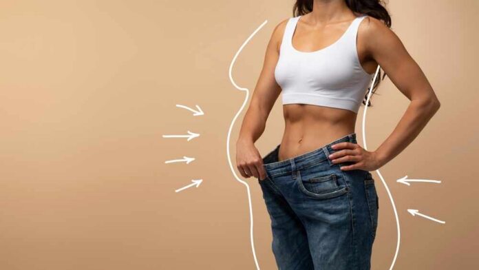 shutterstock_2356487923.jpg Woman showcasing weight loss by holding oversized jeans