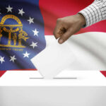Explosive Allegations Rock Georgia GOP Primary A hand placing a ballot into a ballot box with the Georgia state flag in the background