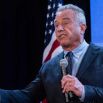RFK Jr. Targets SSRIs in Federal Campaign A man speaking into a microphone at a podium with an American flag in the background