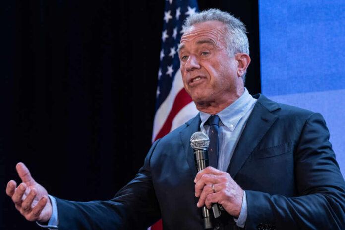 A man speaking into a microphone at a podium with an American flag in the background