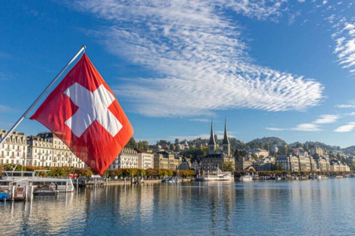 Swiss flag waving in front of Lake Lucerne with a city skyline in the background