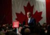 A speaker addressing an audience in front of a large Canadian flag