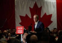 A speaker addressing an audience in front of a large Canadian flag