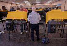 Individuals casting votes at a polling station with electronic voting machines