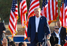 A speaker at a political rally surrounded by American flags and an engaged crowd