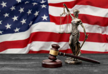 A gavel and a statue of Lady Justice in front of an American flag