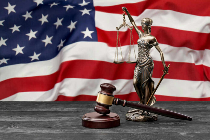 A gavel and a statue of Lady Justice in front of an American flag