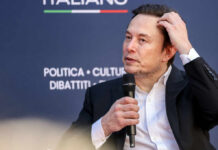 Trillionaire? Musk’s Pricey Mirage Individual speaking at a conference, holding a microphone