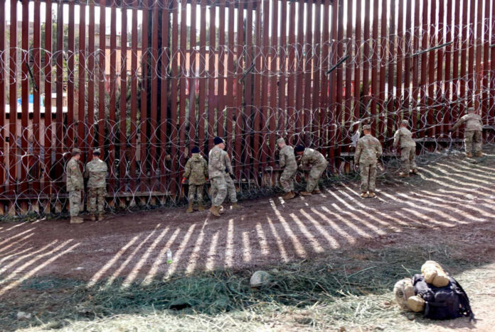 Military personnel working on a border fence with barbed wire