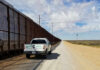 Border Build DRAMA: Dates Keep Moving Border patrol vehicle parked beside a security fence in a desert area
