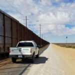 Border patrol vehicle parked beside a security fence in a desert area