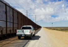 Border patrol vehicle parked beside a security fence in a desert area