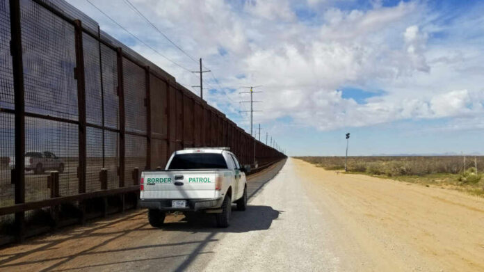 Border patrol vehicle parked beside a security fence in a desert area
