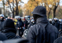 A crowd of masked individuals facing law enforcement in an autumn setting