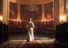 A religious figure standing in a church with candlelight and historic artwork