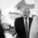 A political figure speaking outdoors in front of an airplane