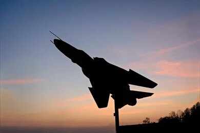 2423058107 Silhouette of a fighter jet mounted on a pedestal at sunset
