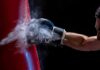 Boxer’s gloved fist strikes a red punching bag, sending chalk dust into the air