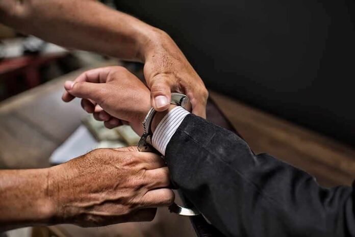 shutterstock_1146300836 hands placing handcuffs on a suited person's wrists