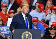 A speaker at a political rally smiling in front of an enthusiastic crowd wearing red hats