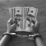 Hands in handcuffs holding stacks of cash