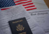 A passport and birth certificate on a table with an American flag in the background
