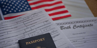 A passport and birth certificate on a table with an American flag in the background