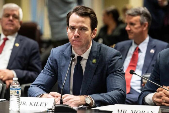 A man in a suit sitting at a table during a government hearing