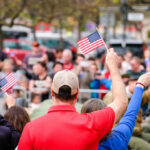 Congressman’s Lobster Jab Ignites Fury Crowd of people waving small American flags at a public event