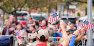 Crowd of people waving small American flags at a public event