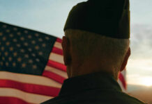 103-Year-Old War Hero Stuns Shelter A veteran in uniform standing in front of an American flag during sunset