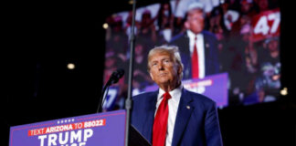 A man in a suit stands at a podium with a microphone during a political rally
