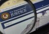 Crypto Mogul’s Muscle: Deputy Caught Lying Close-up view of the U.S. Department of Justice website through a magnifying glass