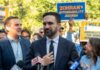 $203K DOE Hire Sparks Patronage Uproar A politician speaking at a rally with supporters holding signs